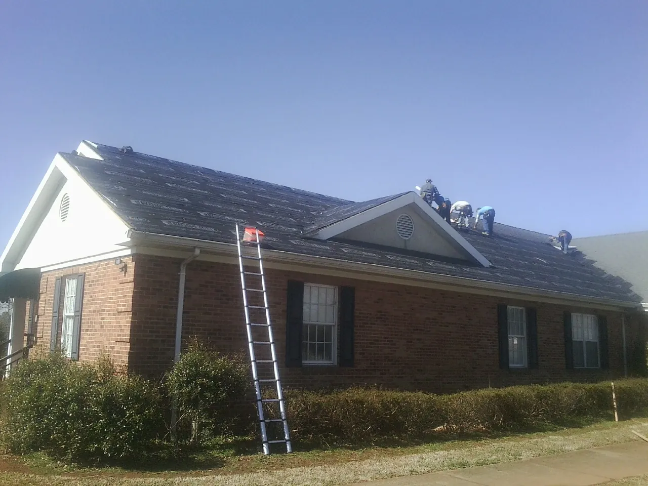 Crew tearing shingles off a brick ranch roof with a ladder set — Metal Roof Repair work by our crew in Markham