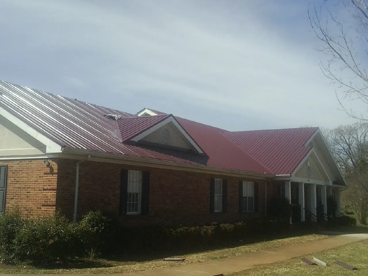 Red metal roof with gabled entries on a long brick building, from a Hail Damage Roof Repair job in Markham